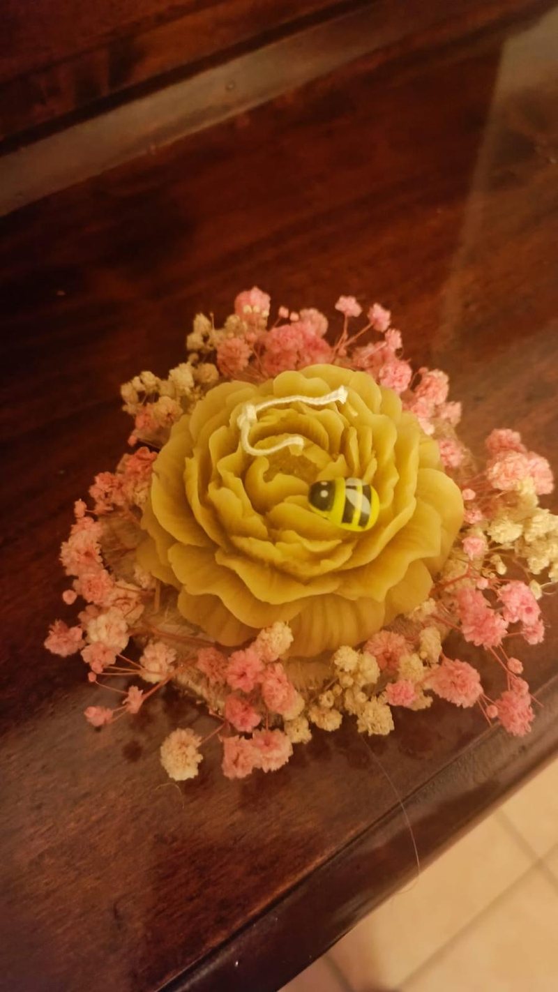 Candela in cera d'api a forma di rosa, con un'ape decorativa, su un letto di fiori secchi