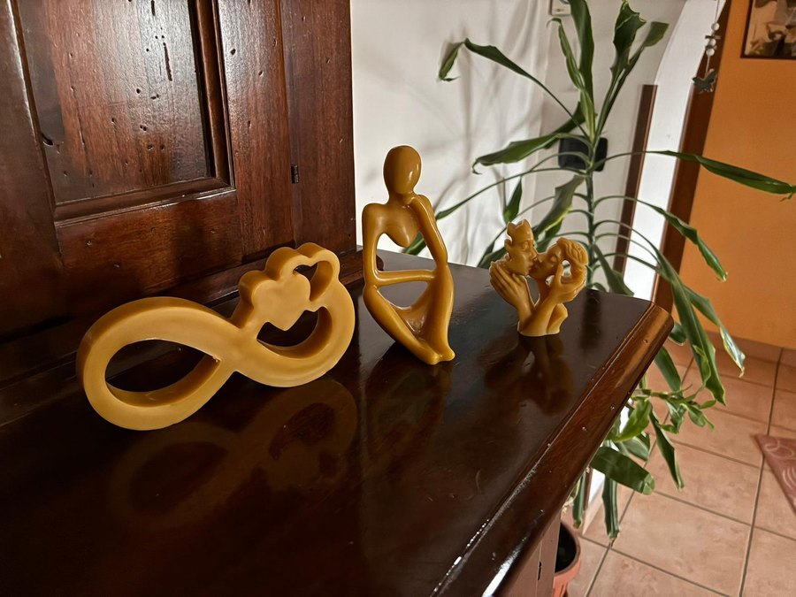 Tre sculture in cera d'api: il simbolo dell'infinito con due cuori, una figura seduta e due volti che si baciano